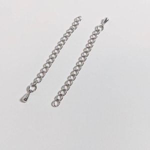 May include: Two silver chain extenders with a lobster clasp on one end and a teardrop-shaped clasp on the other end.