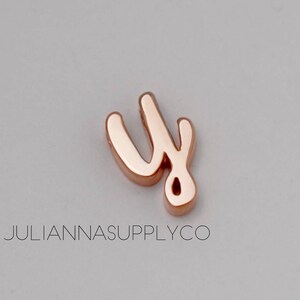 May include: A rose gold charm in the shape of the letter "y" in a cursive script font.