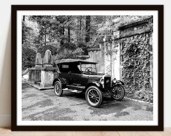 May include: A black and white photograph of a vintage Ford Model T touring car parked in front of a stone wall covered in ivy. The car is in good condition and has a classic look.