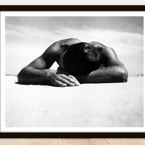 May include: A black and white photograph of a person lying face down on a sandy beach. The person's head is resting on their arms, and their body is relaxed.
