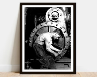 Könnte beinhalten: Schwarzweißfoto eines Mannes, der an einer großen Industriemaschine arbeitet. Er trägt ein Tanktop und eine Arbeitshose und verwendet einen Schraubenschlüssel, um eine Schraube festzuziehen.