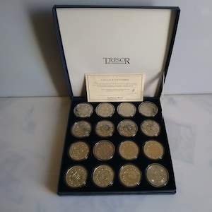Puede incluir: Una caja de terciopelo azul que contiene una colección de 20 monedas de plata. Las monedas están dispuestas en forma de cuadrícula y todas son del mismo tamaño. La caja tiene un certificado de autenticidad que dice "Tresor du Patrimoine" y "Collection de 10 ECU europeens".