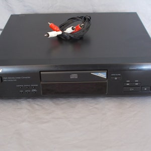 Puede incluir: Un reproductor de CD Sony negro con una pantalla y botones plateados. El reproductor tiene una bandeja de CD abierta y las palabras "High Density Linear Converter" impresas en la parte delantera. El reproductor está conectado a un par de cables RCA rojo y blanco.