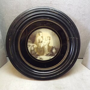 May include: A black framed round picture with a sepia toned image of a woman and two children inside. The image is surrounded by a gold trim.