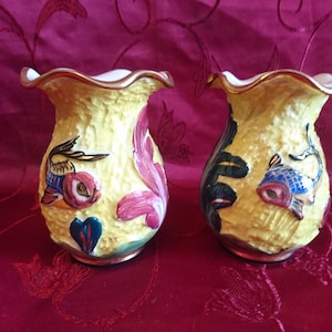 Peut inclure: Deux petits vases en céramique jaune avec une surface texturée. Chaque vase présente un motif de poisson coloré avec des accents roses, bleus et verts. Les vases ont un bord festonné et une bordure dorée.