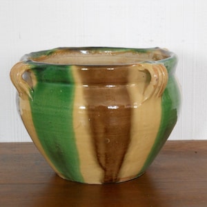 Può includere: Un vaso in ceramica smaltata con strisce verdi, marroni e beige. Il vaso ha due piccole maniglie sui lati.