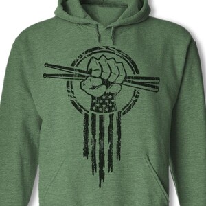 May include: Green hooded sweatshirt with a black and white graphic of a fist holding drumsticks. The fist is holding the drumsticks in a clenched fist position. The graphic is in the shape of an American flag.