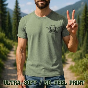 A man wearing a green t-shirt with a skull and crossbones design is making a peace sign with his hands.