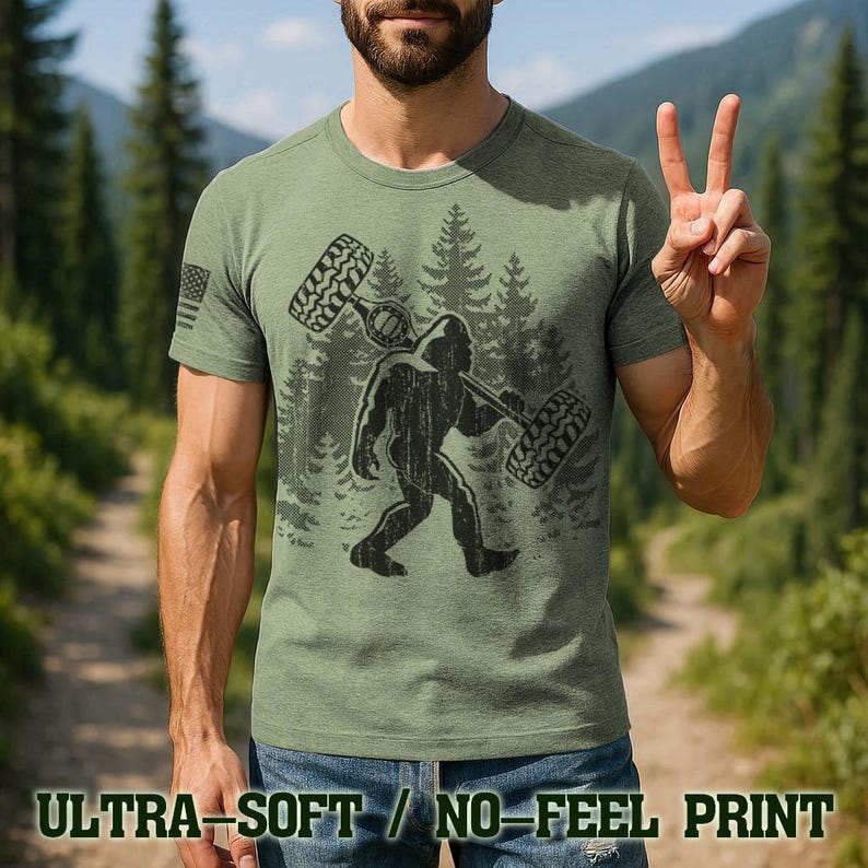 A man wearing a green t-shirt with a graphic of a Sasquatch and tires on it, making a peace sign with his hands.