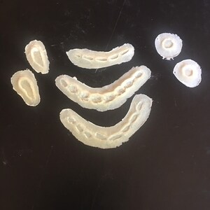 May include: A set of six white silicone molds for making various shapes, including a crescent moon, a circle, and a heart. The molds are on a black surface.