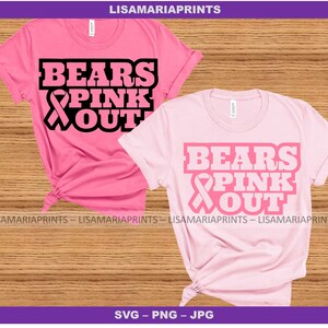 May include: Two pink t-shirts with the text "Bears Pink Out" and a pink ribbon graphic. The shirts are folded and displayed on a woodgrain background.