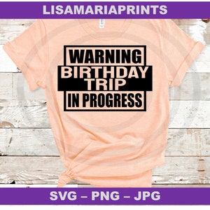Op de afbeelding: Een perzikkleurig T-shirt met zwarte tekst die "WARNING BIRTHDAY TRIP IN PROGRESS" luidt.