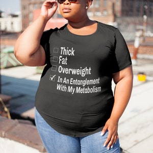 May include: Black t-shirt with a white check list that reads "Thick", "Fat", "Overweight", and "In An Entanglement With My Metabolism". The check mark is next to the last option.