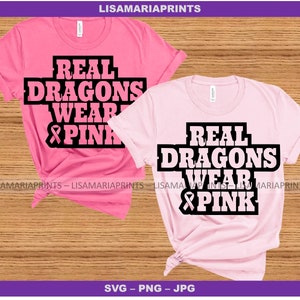 May include: Two pink t-shirts with the text "Real Dragons Wear Pink" and a pink ribbon graphic. The text is in black.