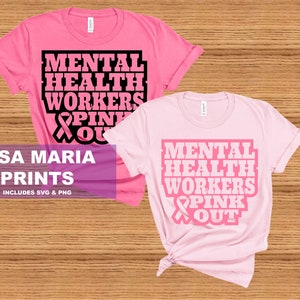 May include: Two pink t-shirts with the text "Mental Health Workers Pink Out" and a pink ribbon graphic. The text is in black and the ribbon is in pink. The shirts are laid out on a wooden surface.