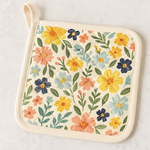 Könnte beinhalten: Quadratischer, gesteppter Topflappen mit cremefarbenem Rand und Aufhängeschlaufe. Das Blumenmuster zeigt gelbe, blaue und pfirsichfarbene Blumen mit grünen Blättern auf cremefarbenem Hintergrund. Der Topflappen ist etwa 20 cm groß.