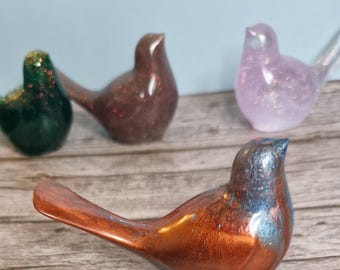 Peut inclure: Une collection de figurines d'oiseaux décoratifs de différentes couleurs. L'oiseau au premier plan est de couleur cuivrée avec des reflets bleus. D'autres oiseaux sont verts, bruns et violets. Les figurines sont sur une surface en bois.