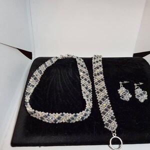 May include: A silver necklace, bracelet, and earrings set with blue and clear crystal beads.