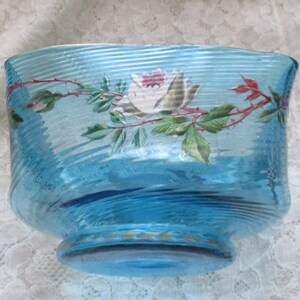 May include: A blue glass bowl with a white rose and green leaves painted on the side. The bowl has a wavy, textured surface.