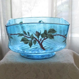 May include: A blue glass bowl with a hand-painted design of a rose vine with thorns. The bowl has a rippled texture and a square shape.