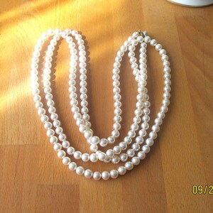 May include: A multi-strand pearl necklace with a silver clasp. The necklace features three strands of round, white pearls, creating a classic and elegant look. The pearls are evenly sized and have a subtle luster, perfect for formal occasions.