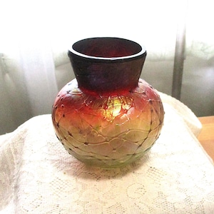 May include: A decorative glass vase with a round body and a flared neck. The vase features a gradient of colors, transitioning from a deep burgundy at the top to a golden-yellow at the base. The surface is textured with a delicate pattern.