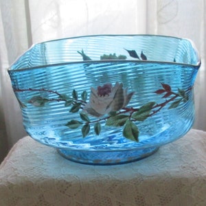 May include: A blue glass bowl with a white rose and green leaves painted on the side. The bowl has a rippled texture.