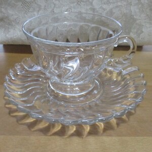 May include: A clear glass teacup and saucer set with a swirl design.