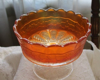May include: A vintage orange iridescent glass bowl with a scalloped rim and a footed base. The bowl has a floral design in the centre.