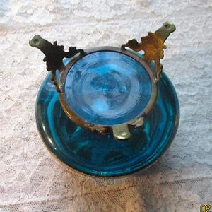 Op de afbeelding: Een vintage turquoise glazen kom met een messing rand en decoratieve details. De kom heeft een ronde vorm en een wervelend patroon in het glas. De messing rand heeft sierlijke details, wat bijdraagt aan de antieke uitstraling.