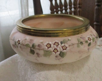 May include: A white ceramic bowl with a gold rim and floral design. The bowl has a pink background with white flowers and green leaves.