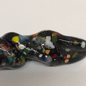 Może przedstawiać: Czarna ceramiczna fajka o skręconym kształcie i powierzchni w kropki. Fajka jest ozdobiona kolorowymi plamkami farby, w tym czerwonymi, niebieskimi, zielonymi, żółtymi i białymi.