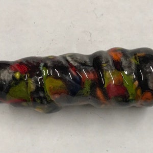 Może przedstawiać: Czarna, zielona, czerwona i biała ceramiczna koralka z wzorem spiralnym.