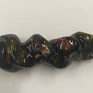 Może przedstawiać: Czarna szklana fajka z wirującym, abstrakcyjnym wzorem w odcieniach zieleni, brązu i pomarańczy.