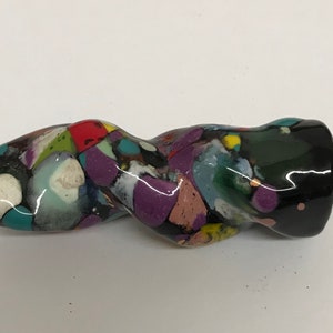Może przedstawiać: Zakręcona, kolorowa fajka ceramiczna z czarną glazurą. Fajka jest ozdobiona różnymi kolorami, w tym czerwonym, zielonym, niebieskim i fioletowym.