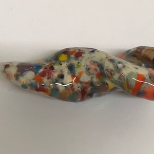 Może przedstawiać: Biała ceramiczna rzeźba o skręconym kształcie i kolorowej, kropkowanej glazurze. Glazura zawiera różne kolory, w tym czerwony, pomarańczowy, żółty, zielony, niebieski i fioletowy.