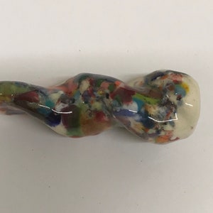 Może przedstawiać: Biała ceramiczna rzeźba o abstrakcyjnym, wirującym kształcie. Rzeźba pokryta jest kolorową, nakrapianą glazurą.