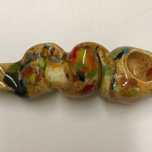 Może przedstawiać: Ceramiczna fajka z brązową, białą i wielokolorową glazurą. Fajka ma kształt węża z miską na końcu.