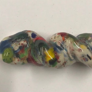 Może przedstawiać: Biała ceramiczna fajka o skręconym kształcie i kolorowej, nakrapianej glazurze. Glazura zawiera odcienie niebieskiego, zielonego, czerwonego, żółtego i czarnego.