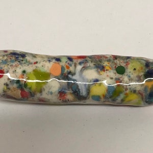 Może przedstawiać: Biała ceramiczna rurka z pstrokatą glazurą w odcieniach czerwonego, pomarańczowego, żółtego, zielonego, niebieskiego i czarnego.