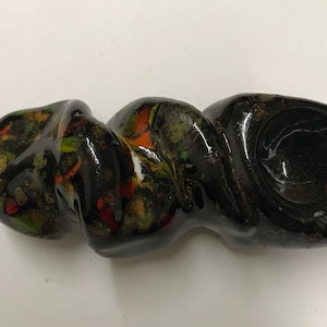 Może przedstawiać: Czarna szklana fajka z wzorem spiralnym i kolorowymi plamkami. Fajka ma czarkę na jednym końcu i ustnik na drugim.