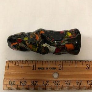 Może przedstawiać: Czarna, pomarańczowa i żółta ceramiczna rzeźba o spiralnym wzorze. Rzeźba ma około 2,5 cm długości.