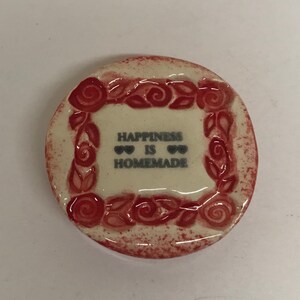 Puede incluir: Un plato de cerámica blanco con un diseño floral rojo y el texto "Happiness is Homemade" con dos pequeños corazones a cada lado de la palabra "is".