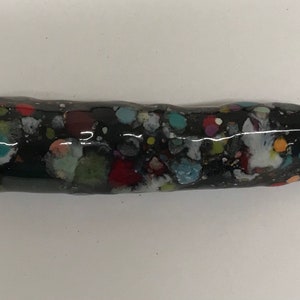 Może przedstawiać: Czarny, podłużny korek do butelki z błyszczącym wykończeniem. Korek jest nakrapiany różnymi kolorami, w tym czerwonym, białym, zielonym i niebieskim. Produkt przeznaczony jest do zamykania butelek.