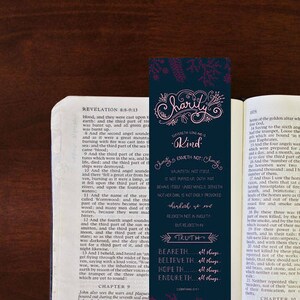 Könnte beinhalten: Ein blaues Lesezeichen mit rosa Schrift, auf dem "Charity" und "Kind" mit einem floralen Design steht. Das Lesezeichen befindet sich in einer geöffneten Bibel mit dem sichtbaren Text "Revelation 9:16-18".