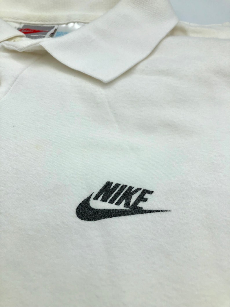 Pu&ograve; includere: Polo bianco con logo Nike nero sul petto.