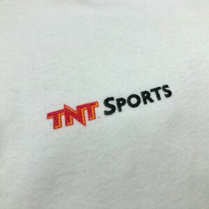 Pu&ograve; includere: Maglietta bianca con un logo "TNT Sports" ricamato in rosso e giallo sul davanti.