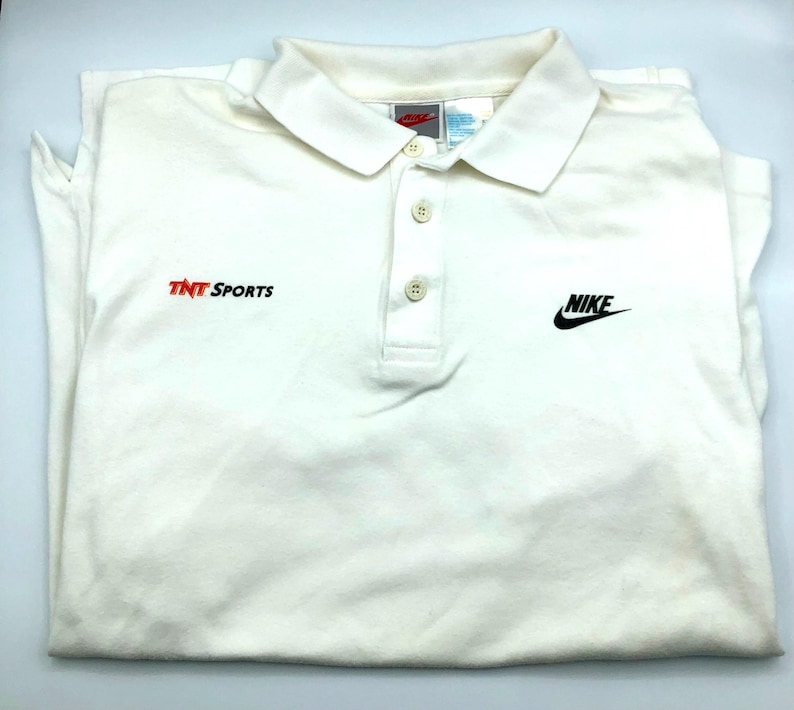 Pu&ograve; includere: Polo a maniche lunghe bianca con logo Nike nero e "TNT Sports" ricamato sul davanti.