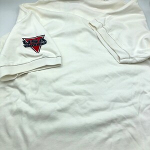 Pu&ograve; includere: Polo bianco con un logo USA Track & Field rosso, bianco e blu sulla manica sinistra.