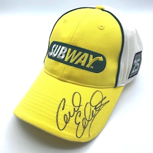 Puede incluir: Gorra de béisbol amarilla con el logotipo de Subway en verde y plata. La gorra tiene una parte trasera de malla blanca y el número 25 en el lateral. La visera tiene una firma negra.